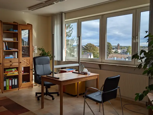 Behandlungszimmer mit Holztisch, Regal und Blick über Troisdorf