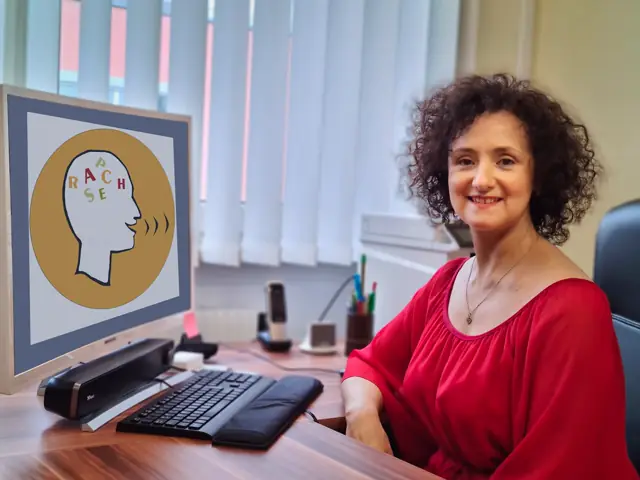 Katerina Passameras am Schreibtisch, auf dem Bildschirm das Logo der Praxis