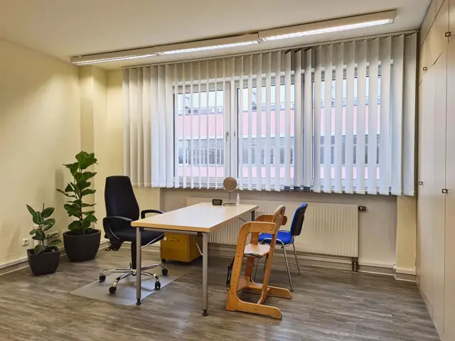 Therapieraum mit Tisch, Kinderhochstuhl und Pflanzen vor einer Fensterfront