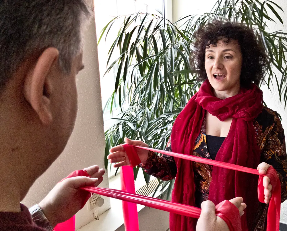 Stimmtherapie: Katerina Passameras übt mit einem Patienten mit einem roten Gymnastikband